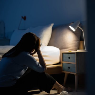 A teenage girl sitting with her head in her hands in a dark bedroom.